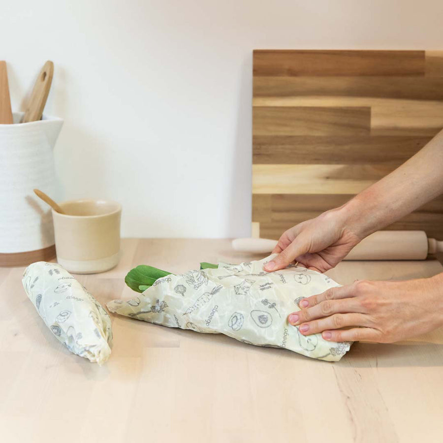 Hands wrapping some green vegetables in a large Abeego plastic-free beeswax food wrap