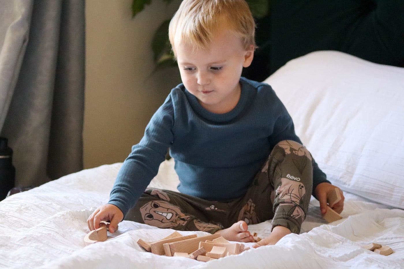 Young boy sat on a white bed playing with the Abel stacking wooden Golden Ratio toy blocks