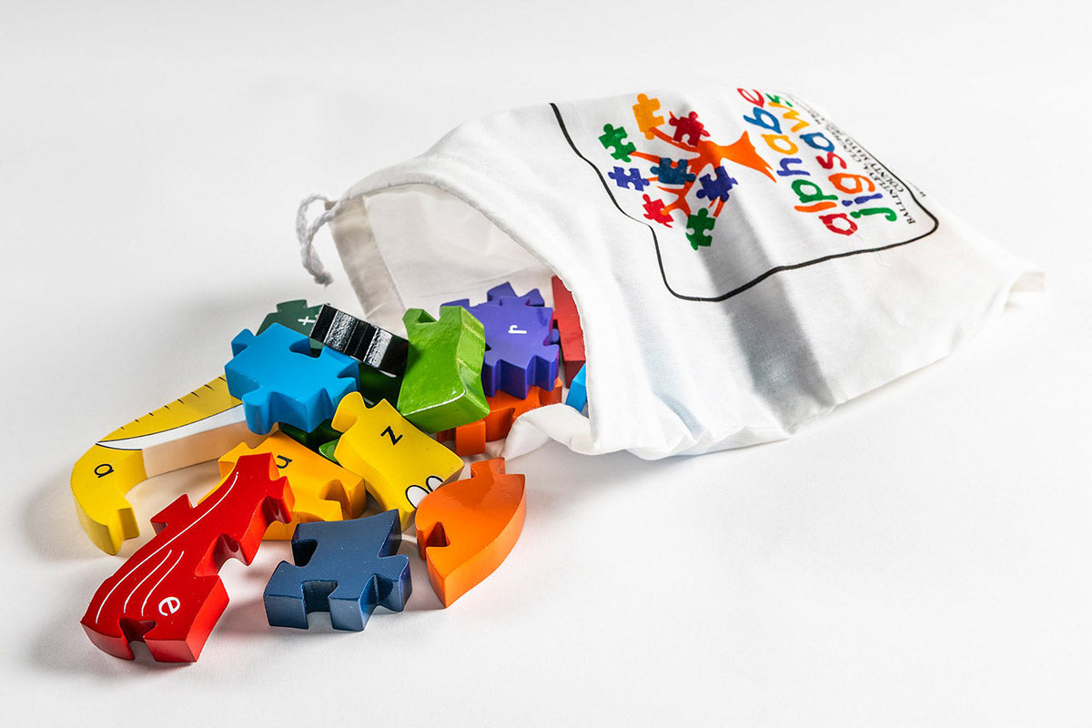 Alphabet Jigsaw Elephant Alphabet wooden jigsaw pieces pouring out of a white drawstring bag on a white background