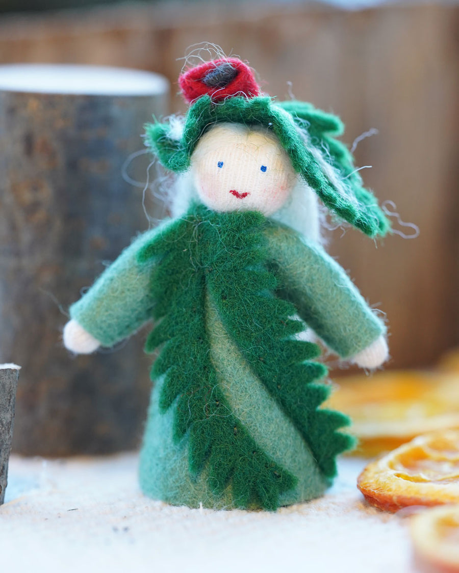 Close up of an Ambrosius yew Christmas fairy figure on a white floor next to some small logs and dried oranges