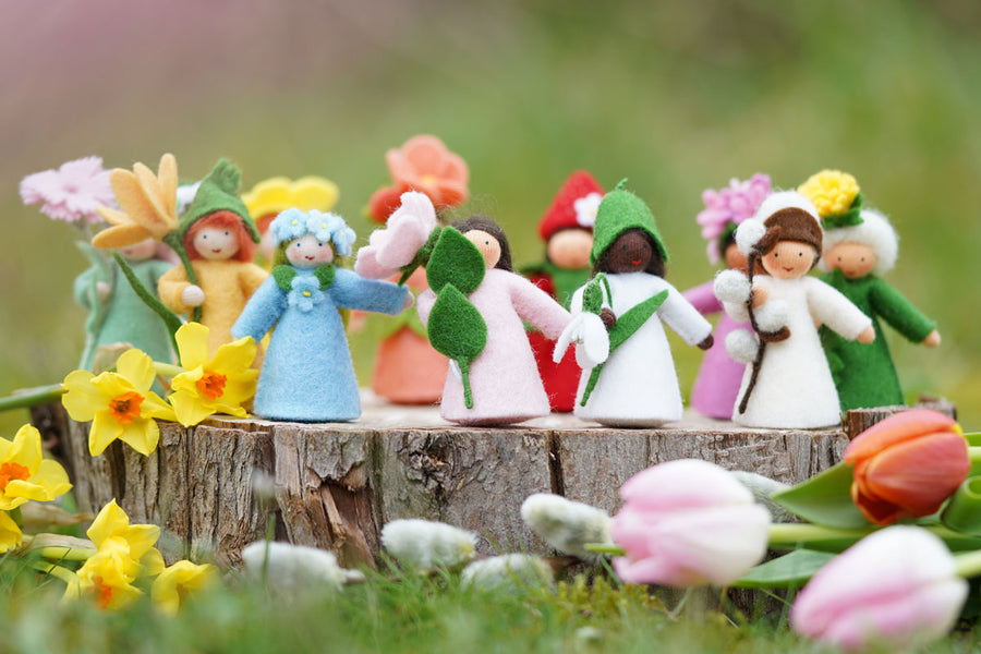 Ambrosius handmade spring felt fairy figures stood on a wooden log next to some yellow and pink flowers