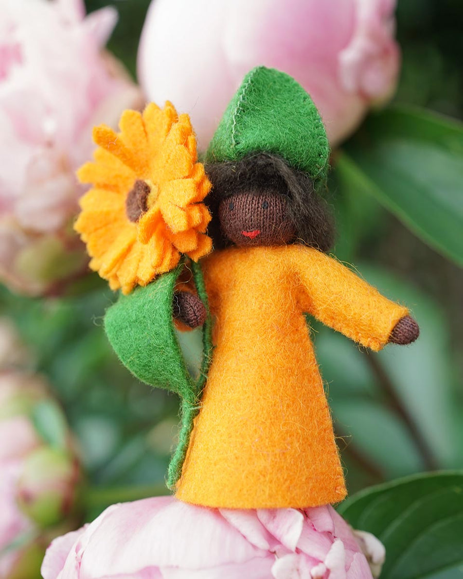 Close up of an eco-friendly Ambrosius orange calendula doll on a pink flower in front of a green plant background