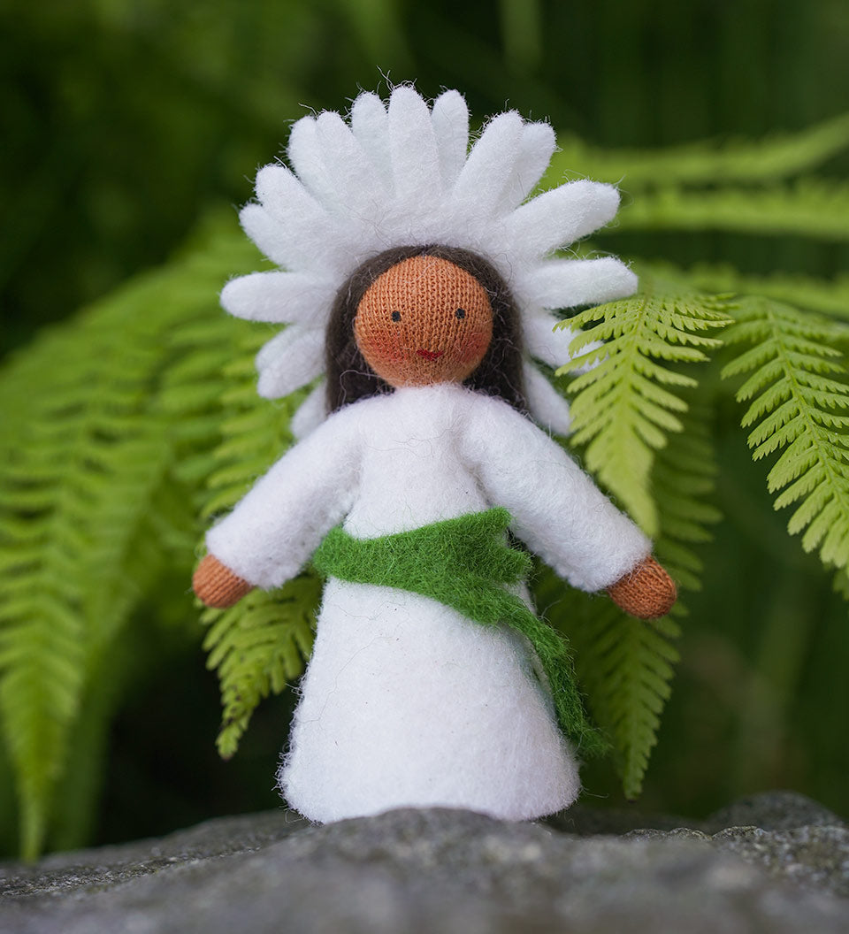 Close up of the Ambrosius oxeye daisy crown fairy doll on a rock in front of a green plant background