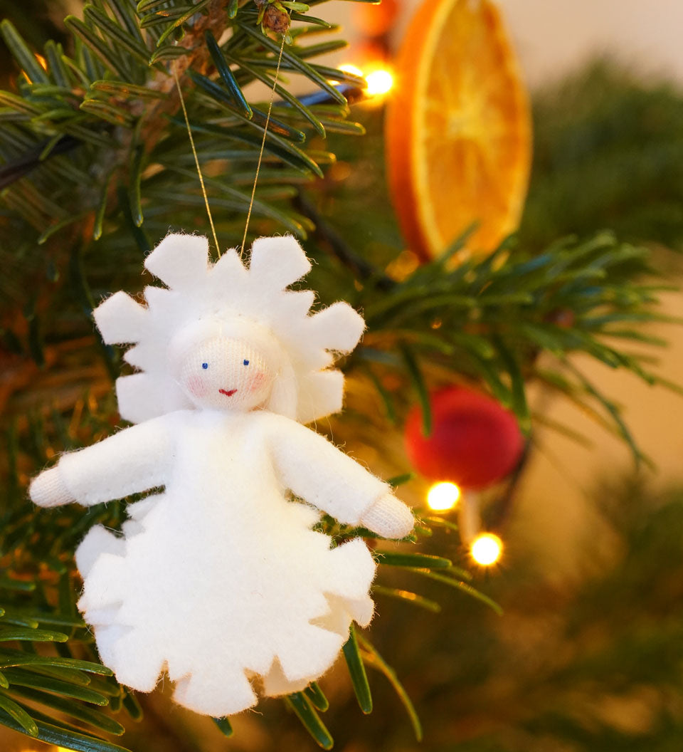 Ambrosius handmade felt snow crystal figure hanging in a Christmas tree in front of a slice of dried orange