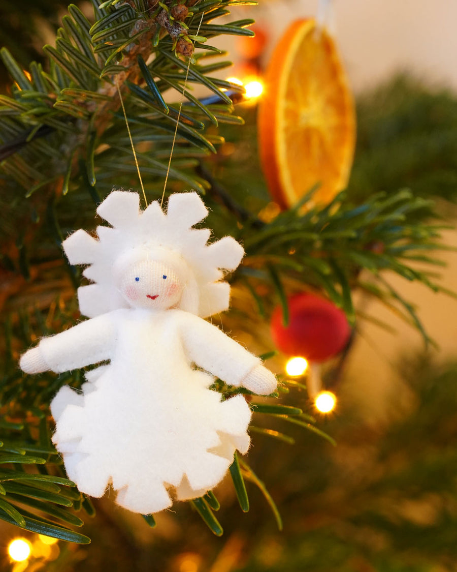 Ambrosius handmade felt snow crystal figure hanging in a Christmas tree in front of a slice of dried orange