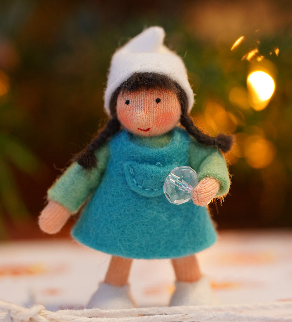 Ambrosius handmade felt winter dwarf girl figure in front of some blurry lights on a white floor