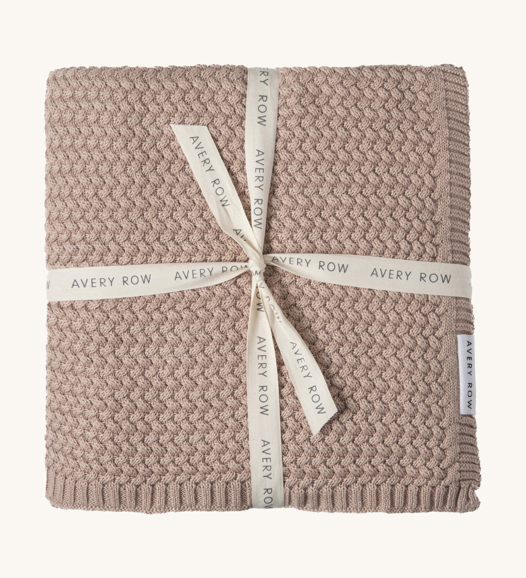 A soft dusty pink plait knitted Avery Row blanket on a cream background.