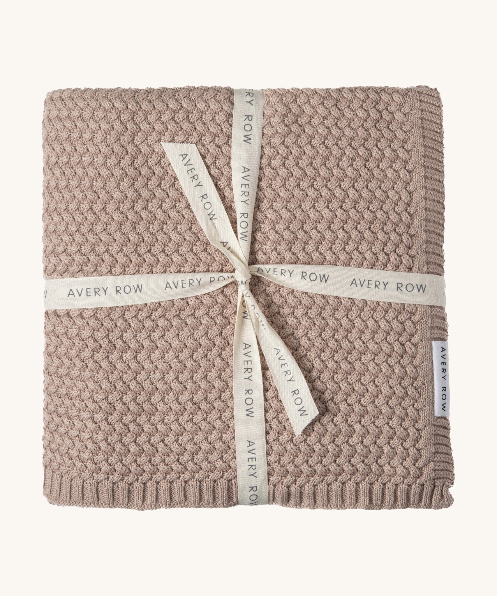 A soft dusty pink plait knitted Avery Row blanket on a cream background.