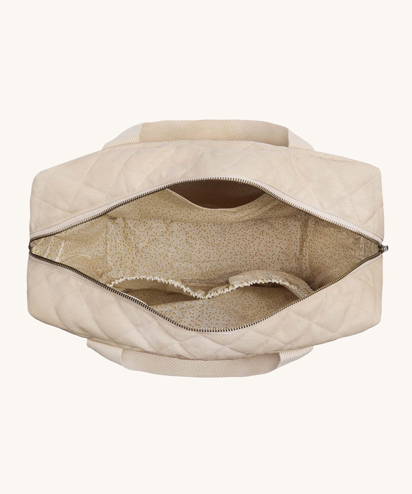 An overhead view of the Avery Row Baby Changing Bag in a  Natural colour showing the chamomile print sateen lining and inner pockets.