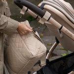 Close up of any adults hand about to attach the Avery Row Baby Changing Bag in a  Natural colour to a pram using the pram clips that are included