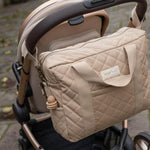 A Avery Row Baby Changing Bag in a  Natural colour shown attached to a pram with the pram clips that are included 