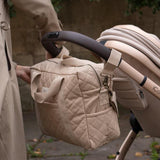 A Avery Row Baby Changing Bag in a  Natural colour shown attached to a pram with the pram clips that are included 