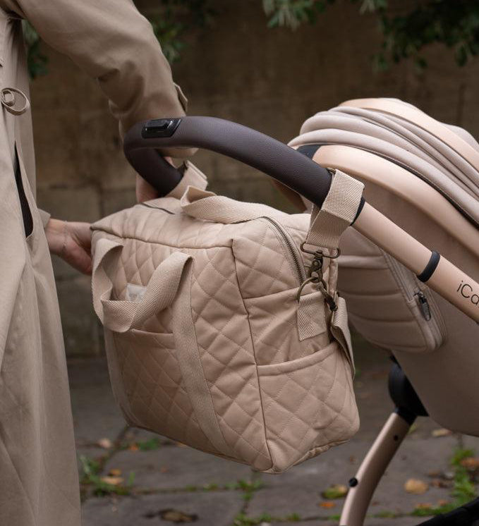 A Avery Row Baby Changing Bag in a  Natural colour shown attached to a pram with the pram clips that are included 