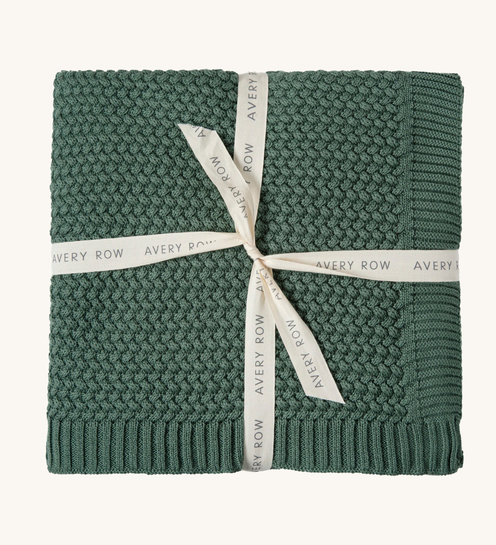 A pine green Avery Row knitted blanket on a cream background