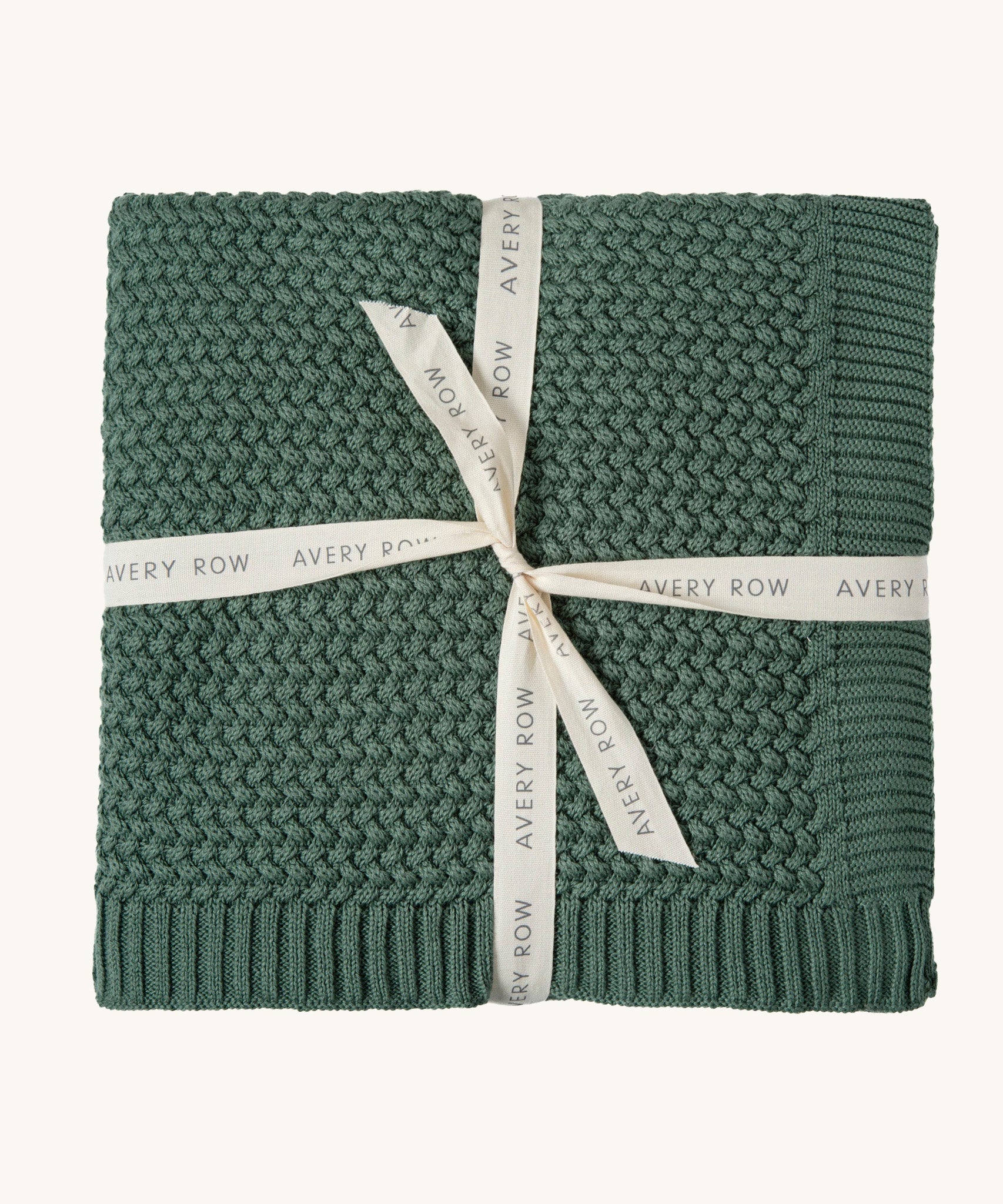 A pine green Avery Row knitted blanket on a cream background