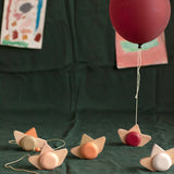 Babai sustainable wooden pull and go ship toys spread out on a green sheet below a red balloon