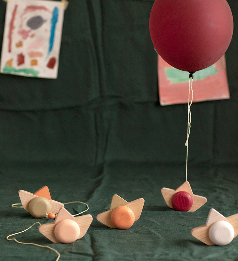 Babai sustainable wooden pull and go ship toys spread out on a green sheet below a red balloon