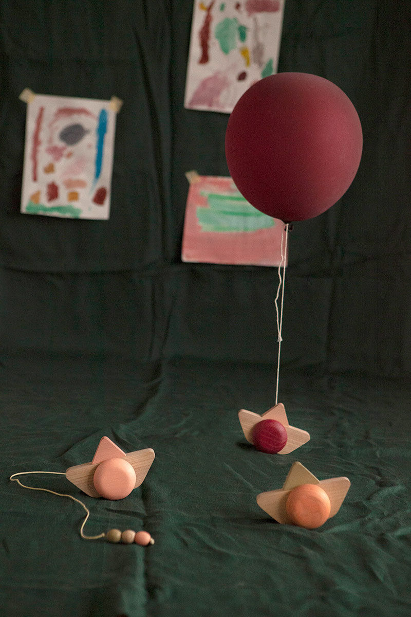 Babai sustainable wooden pull and go ship toys spread out on a green sheet below a red balloon