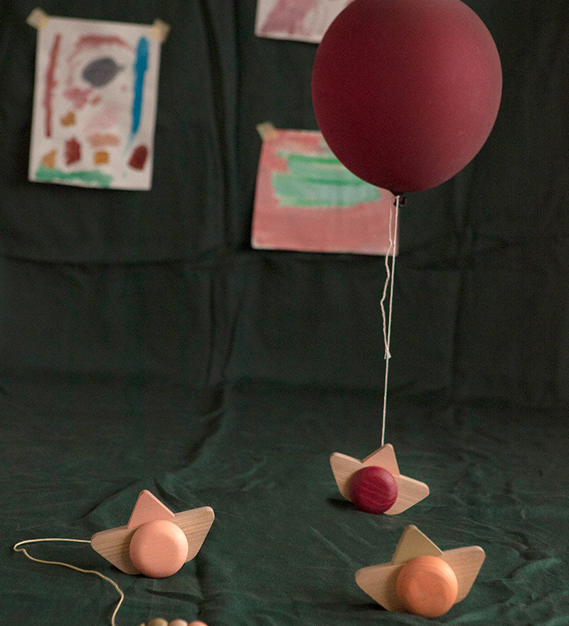 Babai sustainable wooden pull and go ship toys spread out on a green sheet below a red balloon