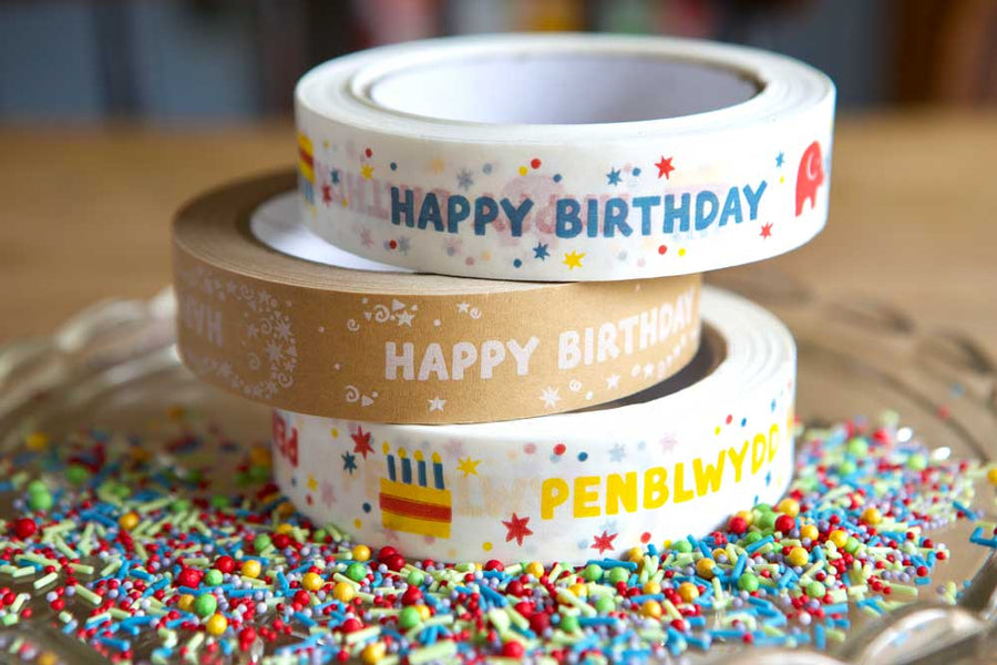 Stack of three babipur design eco paper tapes including colourful and kraft English Happy Birthday designs and Colourful Welsh Penblwydd Hapus design