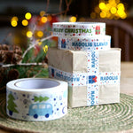 A box wrapped in brown paper and Christmas Nadolig Llawen tape. There are rolls of Christmas tape surrounding the box.