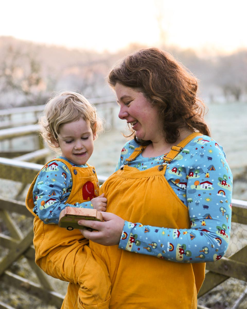 Woman carrying a little boy wearing matching Babipur x Frugi eco-friendly childrens and adults Babipur World tops