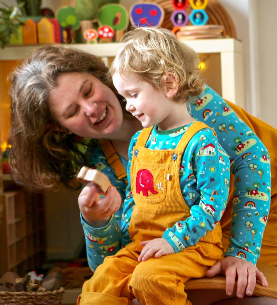 Woman and boy sat in a room playing and wearing matching Babipur x Frugi organic cotton Babipur world tops