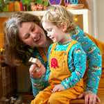 Woman and boy sat in a room playing and wearing matching Babipur x Frugi organic cotton Babipur world tops