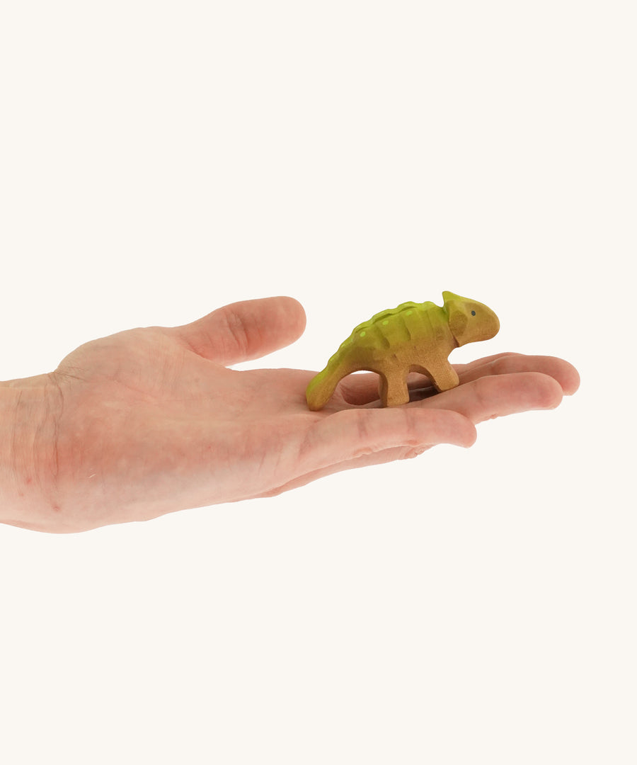 Green and light brown baby standing Akylosaurus on a hand