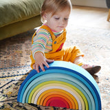 A child sitting besides the Grimm's Gwawr Sunrise 12 Piece Rainbow. The child is reaching for the biggest blue arch.