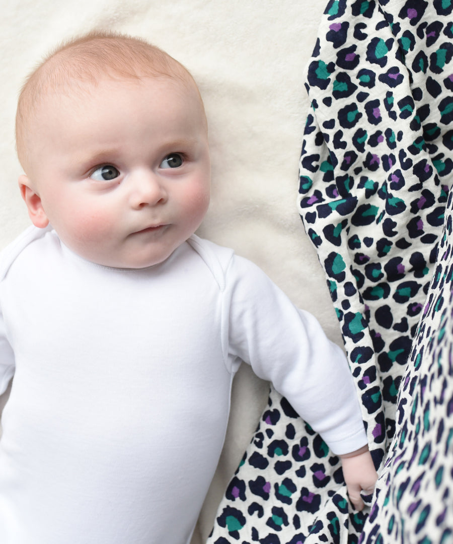 A baby looking up towards the Etta Loves Extra Large Organic Cotton Baby Muslin Square - Purple Leopard next to them. The image shows the vibrancy of the colours