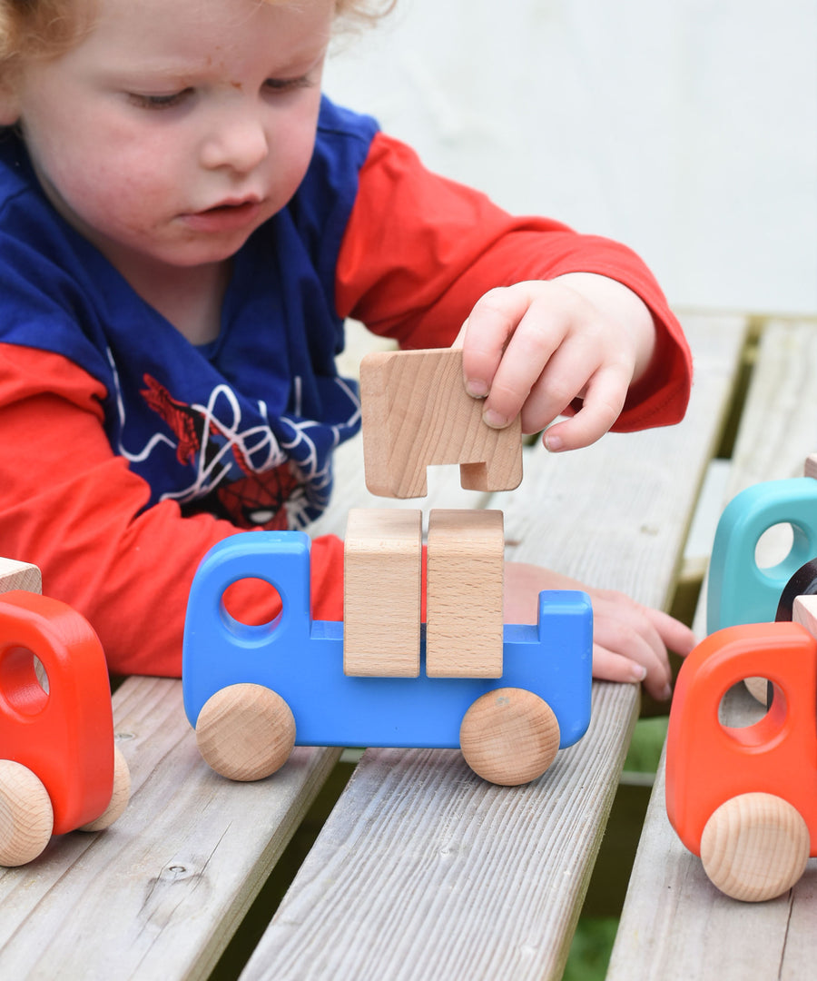 A child placing the wooden blocks on the back on a blue Bajo truck