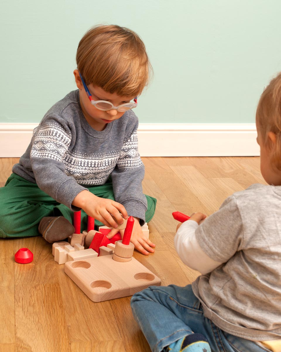 Two children sat on a wooden floor playing with the Bajo plastic-free castle stacking toy