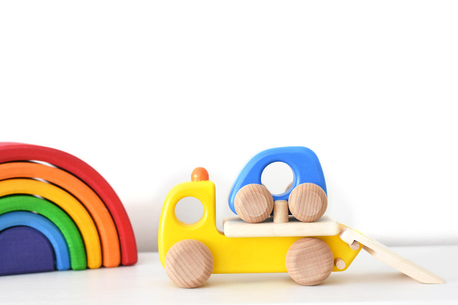 Bajo children's wooden tow truck toy on a white table next to a Grimms mini rainbow toy