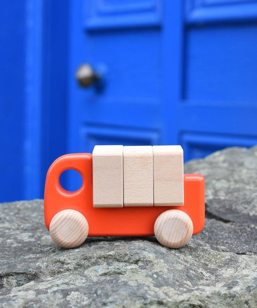 A coral coloured Bajo truck with blocks placed on a stone wall 