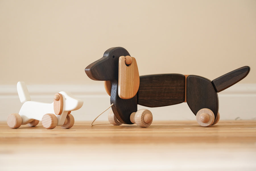 Bajo wooden dachshund puppy toy next to a pull along dachshund figure on a wooden floor