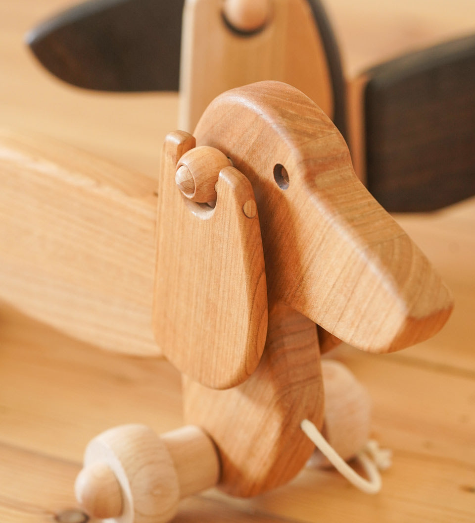 Close up of the handmade natural wooden pull along Bajo dachshund dog on a wooden floor