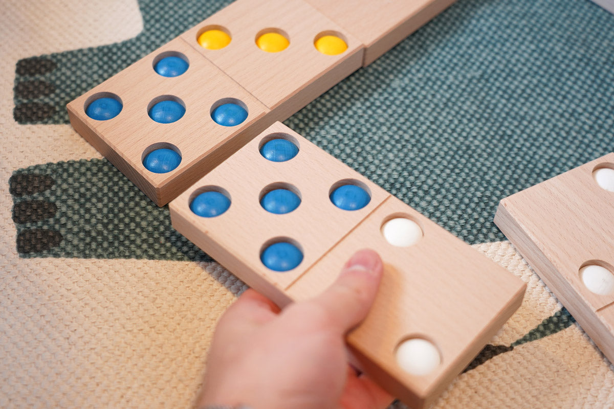 Close up of a hand moving a Bajo XXL wooden domino piece on a blue and white carpet