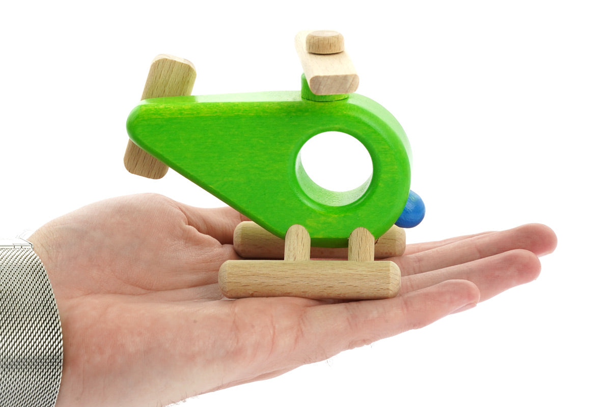 Close up of a Bajo wooden helicopter toy in the palm of a hand on a white background