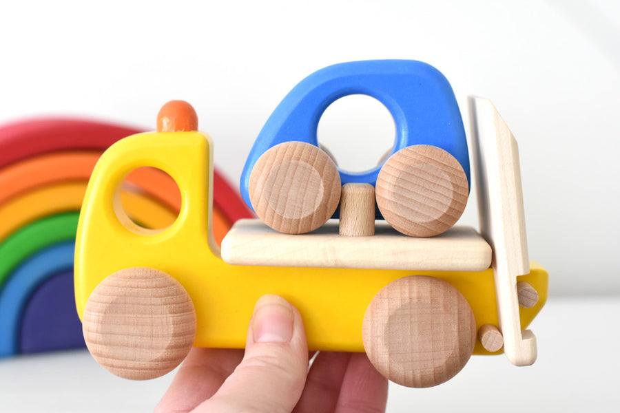 Bajo children's wooden tow truck toy on a white table next to a Grimms mini rainbow toy