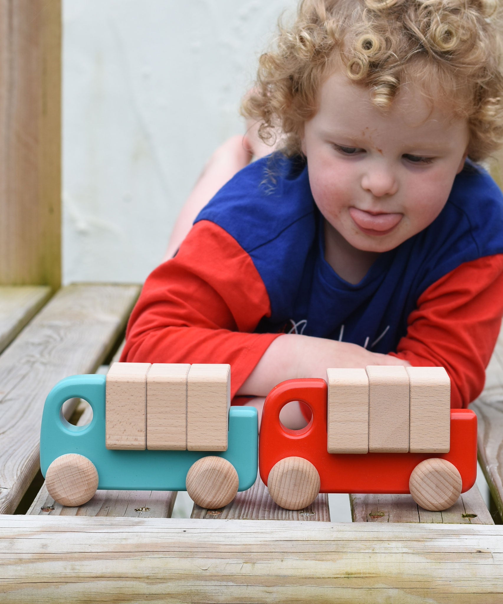 A child playing with a light blue and red Bajo trucks. 