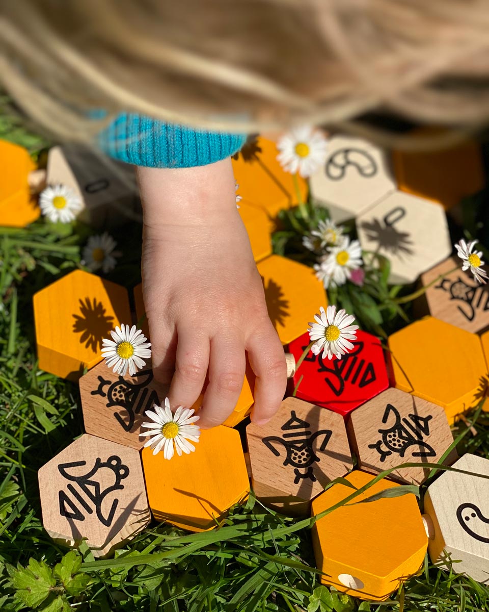 Close up of a child's hand playing with the Bajo wooden hive block toys next to some white flowers