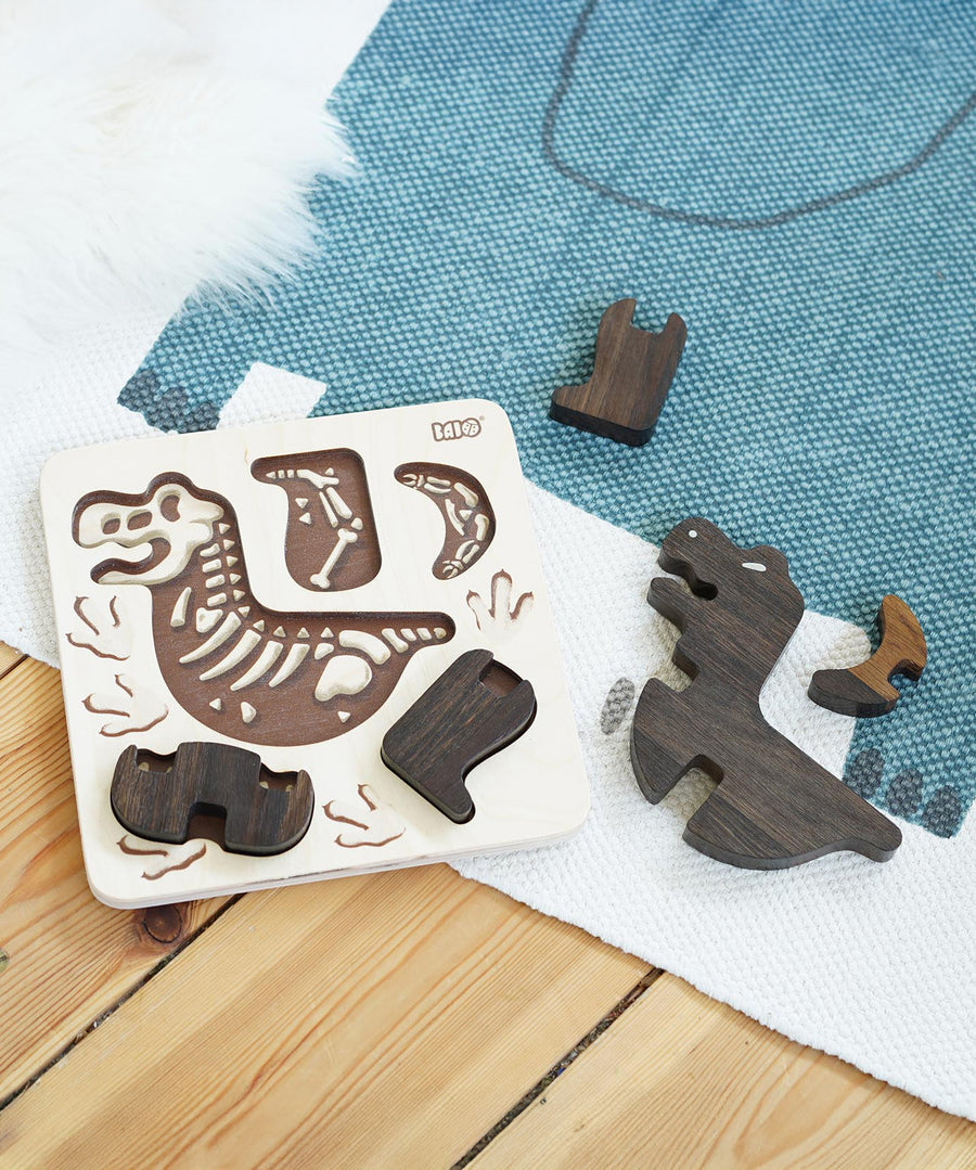 The Bajo Puzzle & Sorter - Black Oak T-Rex laid on a white and blue rug, with some parts in the puzzle board and other parts scattered next on the rug