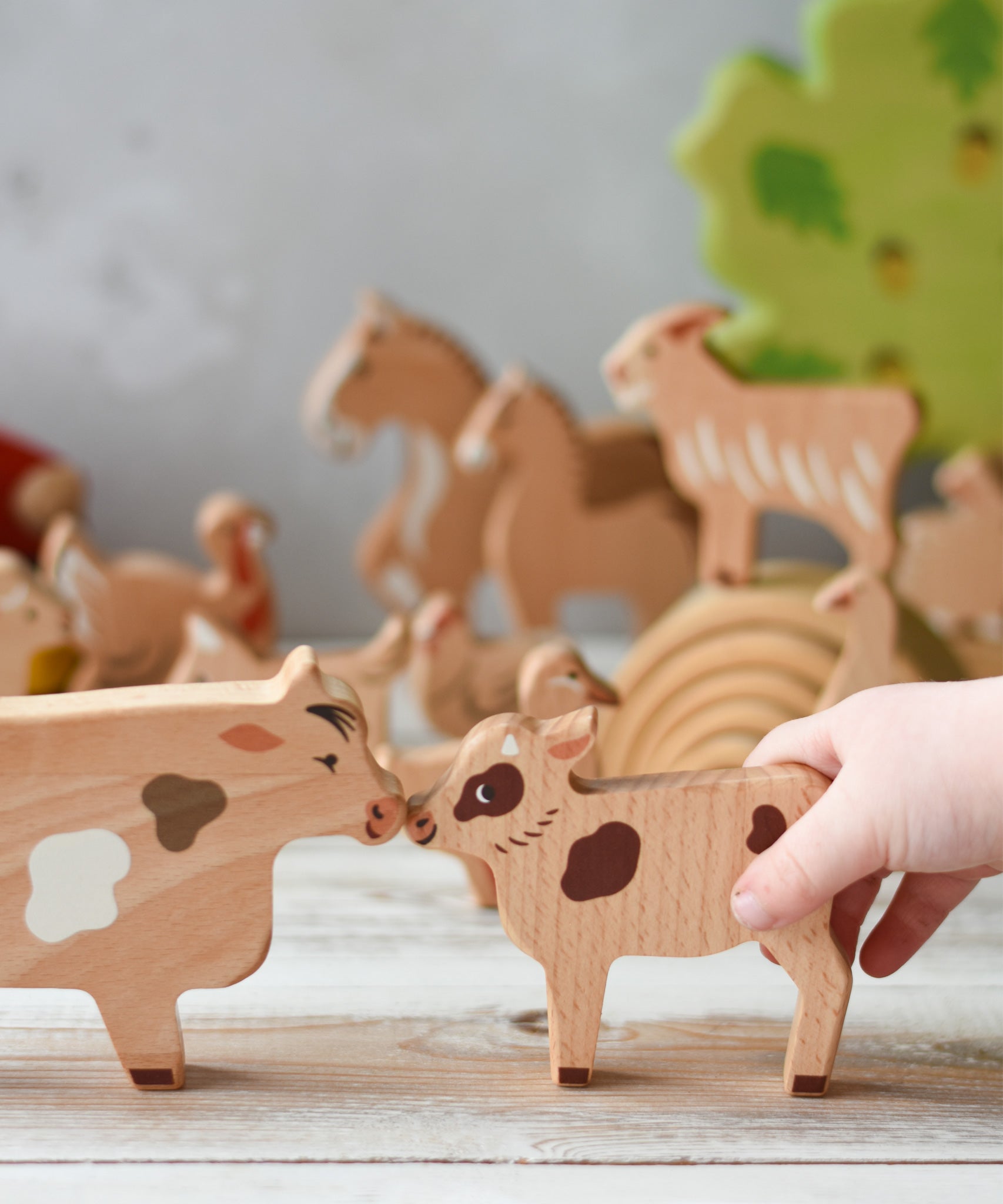 A child's hand holding the calf figure  from the Bajo farm animals set. Other animal figures can be seen in the background.