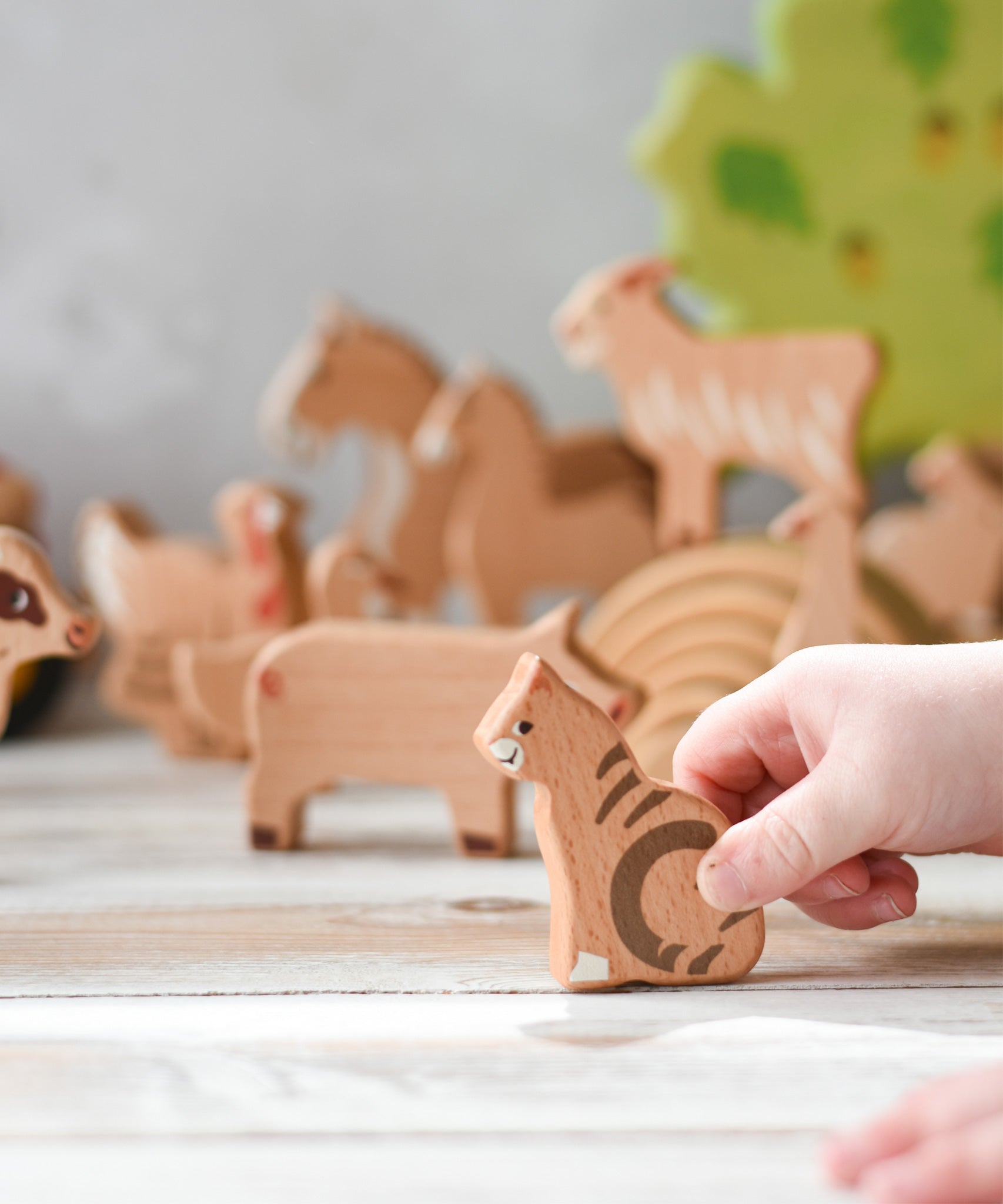 A child's hand holding the cat figure  from the Bajo farm animals set. Other animal figures can be seen in the background.