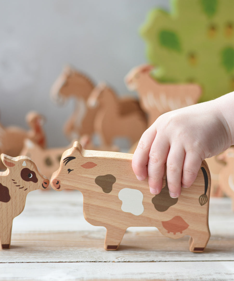 A child's hand holding the cow figure  from the Bajo farm animals set. Other animal figures can be seen in the background.