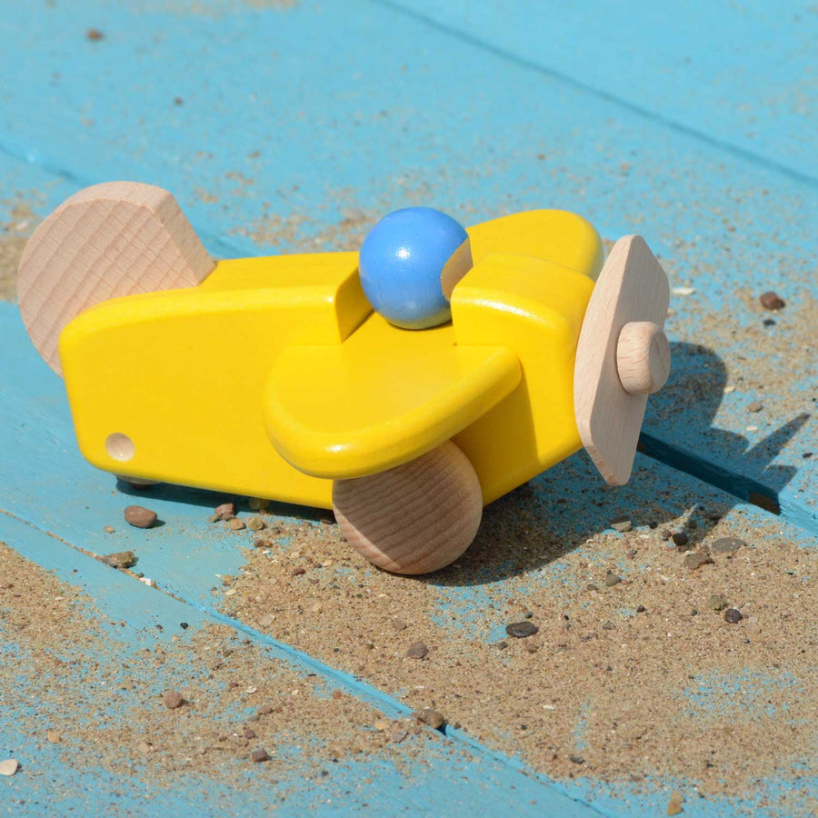 A Bajo Plane With Pilot in a yellow colour way placed on a blue coloured wooden surface in the sunshine. Sand is scattered around the plane