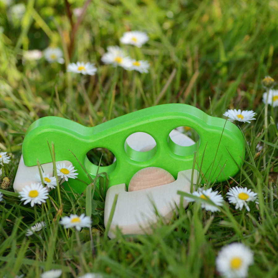 A Bajo airplane in a green colour placed on grass outdoors surrounded by daisies