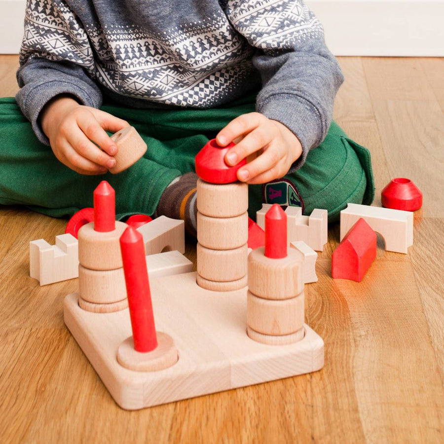 Child sat on a wooden floor playing with the Bajo wooden stacking castle blocks