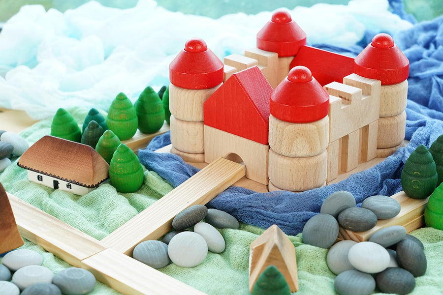 Bajo Castle Stacker toy on some green and blue fabric surrounded by Bumbu wooden houses and some Grapat mandala trees